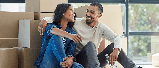 Couple smiling, sitting among moving boxes.